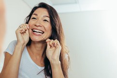 Woman smiling while flossing her teeth in bathroom