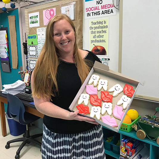 Smiling woman in classroom holding cookies shaped like teeth