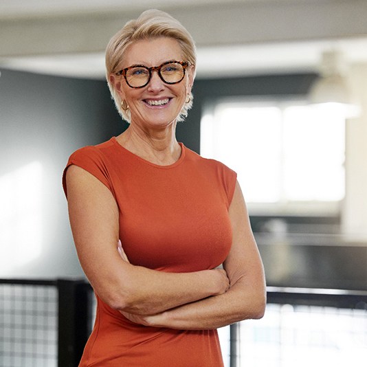 Woman with glasses and orange shirt smiling with arms folded