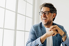 Older man with business jacket looking out window and smiling