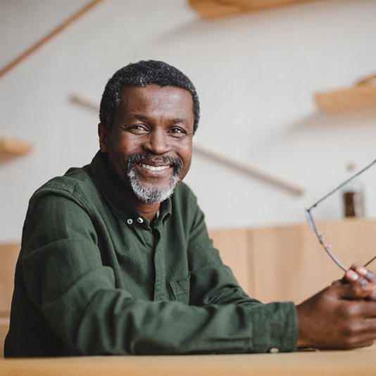 older man smiling while holding glasses