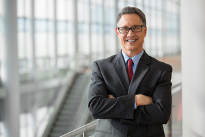 Senior man with glasses and suit smiling with arms folded